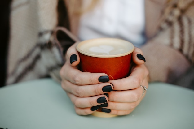 Dos manos femeninas sostienen una taza blanca para llevar con café