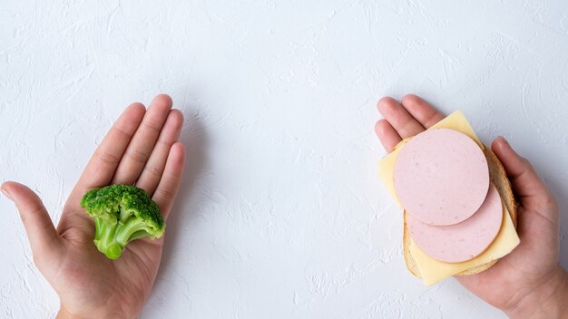 Dos manos sosteniendo brócoli y un sándwich. Idea de comida sana. Fondo claro