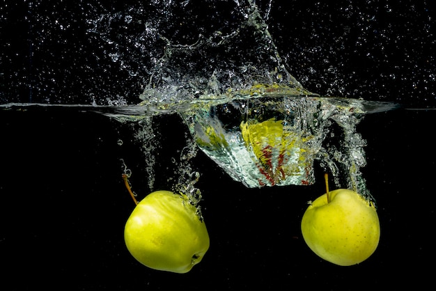 Dos manzana verde salpicaduras en el agua contra el fondo negro