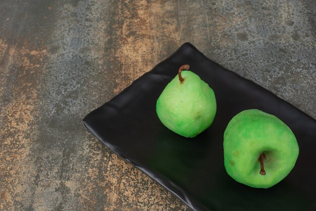 Dos manzanas frescas peladas en un plato oscuro sobre la superficie de mármol.