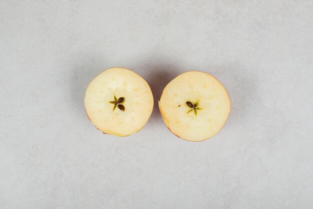 Dos manzanas rojas cortadas por la mitad sobre la superficie gris