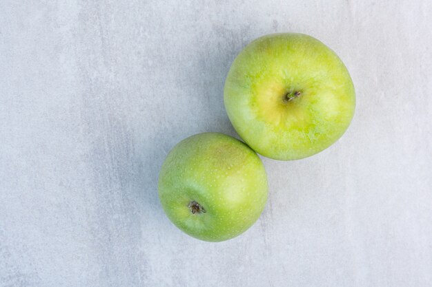 Dos manzanas verdes frescas, sobre el mármol.