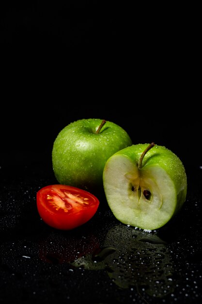 Dos manzanas verdes y tomate en rodajas por la mitad sobre un negro