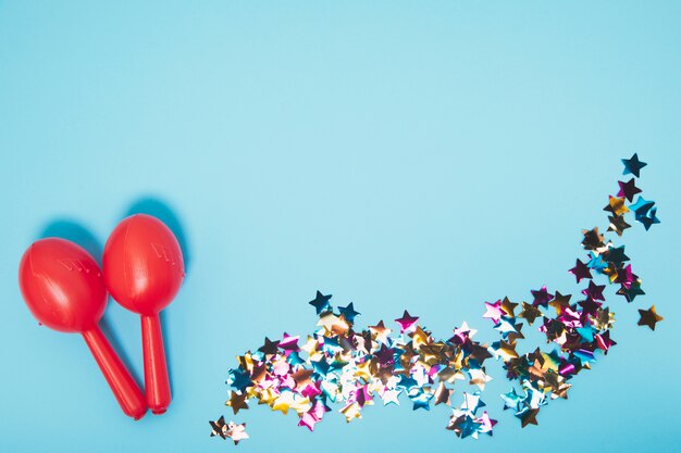 Dos maracas rojas con confeti de forma de estrella de colores sobre fondo azul