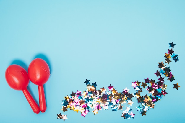 Dos maracas rojas con confeti de forma de estrella de colores sobre fondo azul