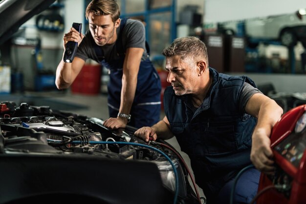 Dos mecánicos que usan compresor mientras trabajan en el sistema de aire acondicionado del automóvil en un taller de reparación de automóviles