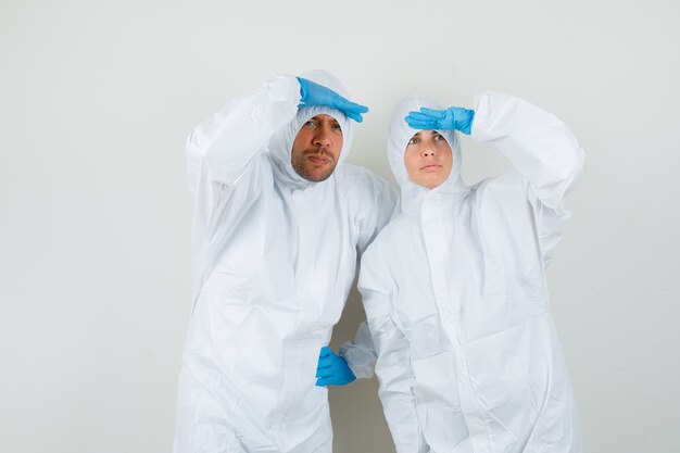 Dos médicos mirando lejos con las manos sobre la cabeza en trajes protectores