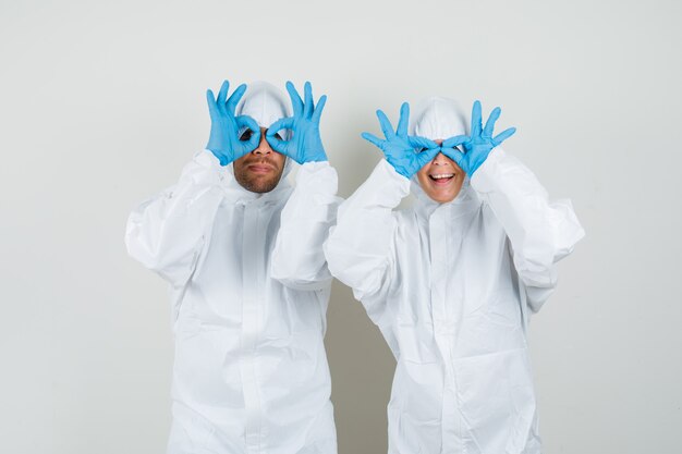 Dos médicos mostrando gesto de gafas en trajes protectores