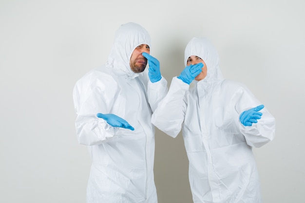Dos médicos pellizcando la nariz debido al mal olor en trajes protectores