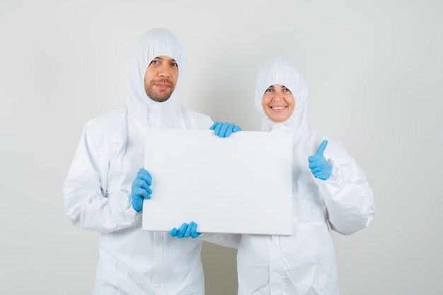 Dos médicos sosteniendo un lienzo en blanco, mostrando el pulgar hacia arriba en trajes de protección