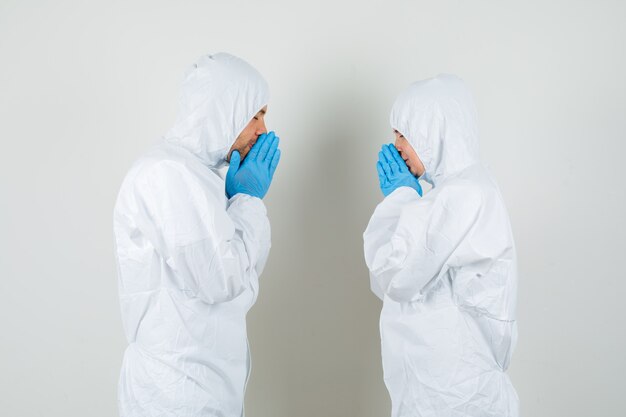 Dos médicos tomados de la mano en gesto de oración en trajes protectores