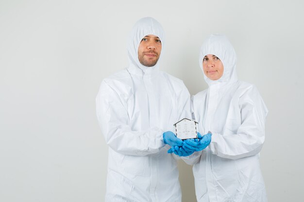 Dos médicos en traje de protección, guantes sosteniendo el modelo de la casa y mirando alegre