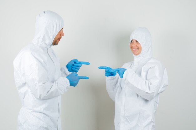 Dos médicos con trajes protectores, guantes apuntando hacia un lado y mirando felices.