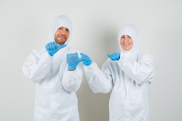 Dos médicos con trajes protectores, guantes apuntando con los pulgares hacia un lado y mirando esperanzados