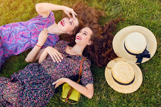 Dos mejores amigas con un colorido vestido boho y cabello rizado tendido sobre la hierba verde