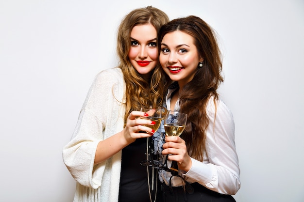 Dos mejores amigas que se divierten en una fiesta en blanco y negro, beben champán sonriendo y chismes, alegres hermanas celebrando la fiesta de cumpleaños, ropa elegante y elegante, fondo blanco.