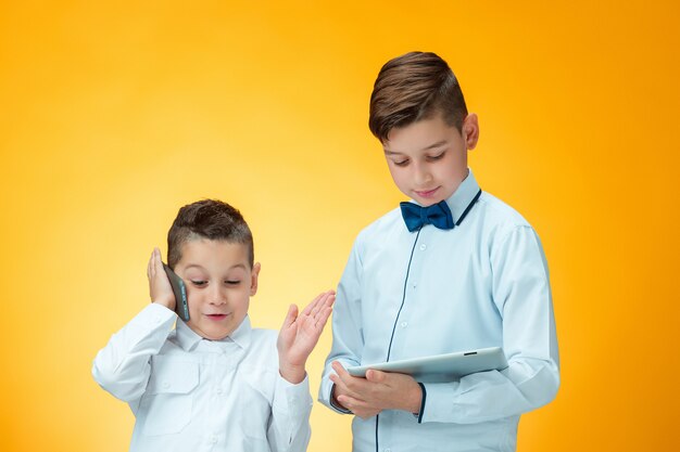 Los dos muchachos usando la computadora portátil en la pared naranja