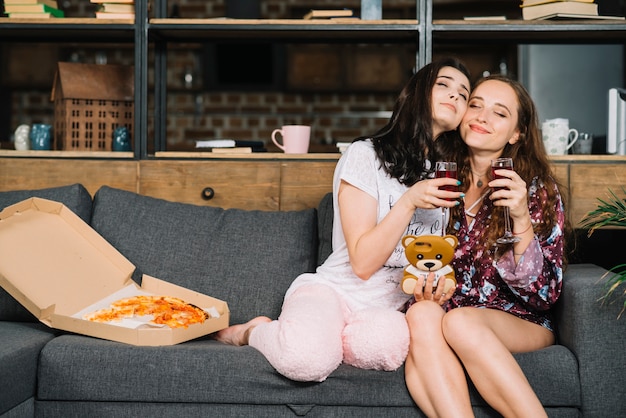 Dos mujeres amistosas que se sientan en el sofá con bebidas