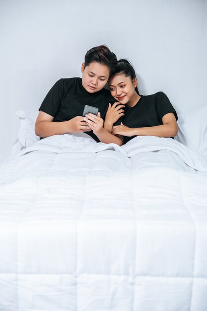 Dos mujeres amorosas durmiendo y jugando teléfonos inteligentes.