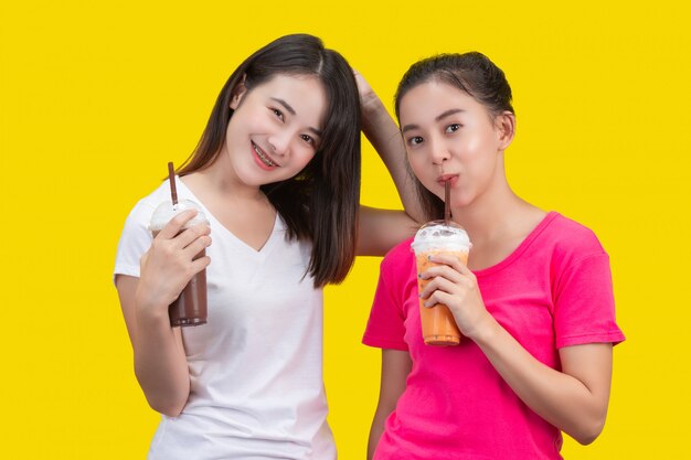 Dos mujeres asiáticas bebiendo té helado de leche y cacao helado en un amarillo.