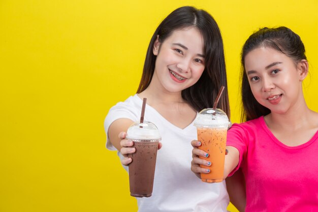 Dos mujeres asiáticas bebiendo té helado de leche y cacao helado en un amarillo.