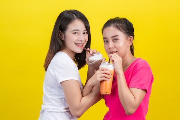 Dos mujeres asiáticas bebiendo té helado de leche y cacao helado en un amarillo.