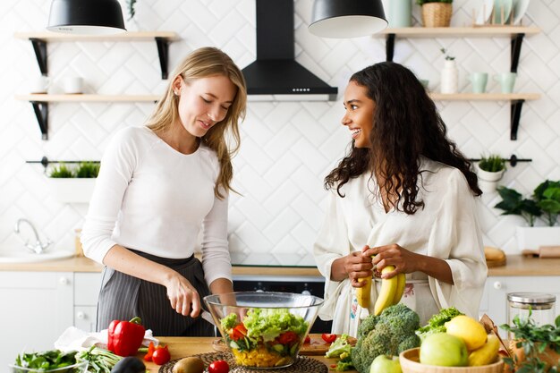 Dos mujeres atractivas en la cocina preparan un desayuno saludable con frutas y verduras.