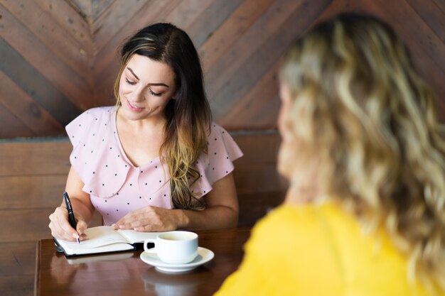 Dos mujeres bebiendo café y tomando notas en el café