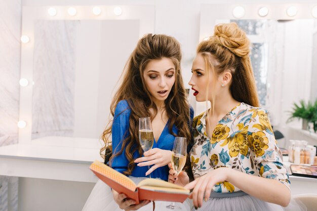 Dos mujeres bonitas asombradas mirando libro en salón de belleza