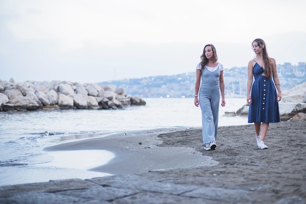 Foto gratuita dos mujeres caminando en la playa de arena