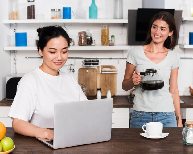 Dos mujeres en casa en la cocina con café y portátil