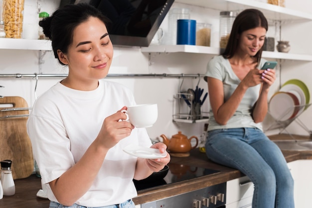 Dos mujeres en casa en la cocina con café y smartphone