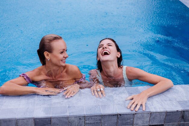 Dos mujeres caucásicas en piscina azul en día lluvioso