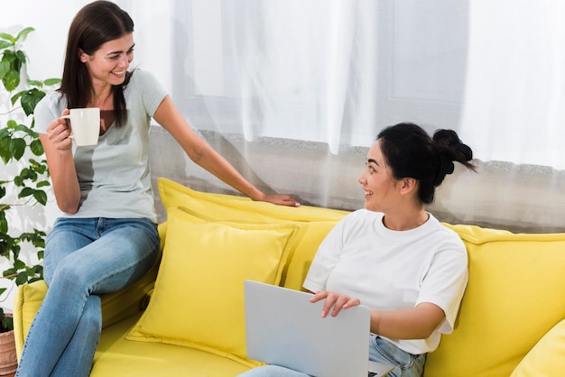 Dos mujeres charlando en casa en el sofá con café y portátil
