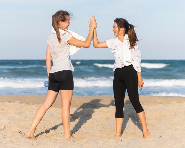 Dos mujeres chocan los cinco mientras hace ejercicio en la playa