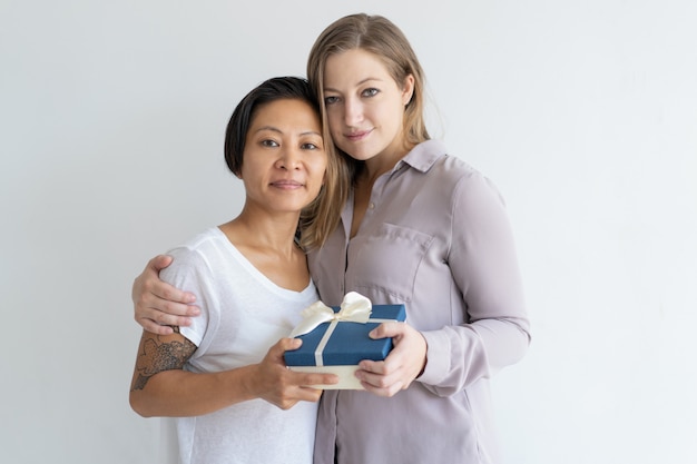 Dos mujeres contentas abrazando y sosteniendo una caja de regalo.