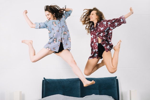 Dos mujeres despreocupadas saltando en la cama