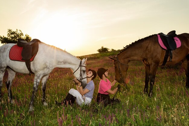 Dos mujeres y dos caballos al aire libre en verano feliz atardecer juntos naturaleza