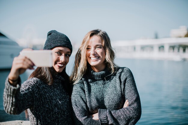 Foto gratuita dos mujeres haciendo un selfie con agua en el fondo