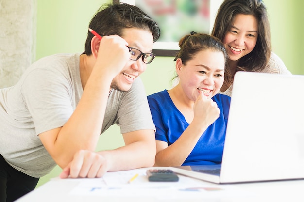 Dos mujeres y un hombre están mirando felizmente la computadora en la oficina moderna