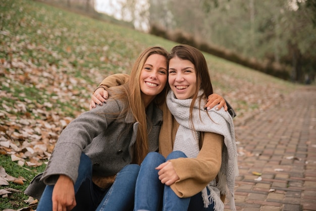 Dos mujeres jóvenes abrazándose y sentados en el parque