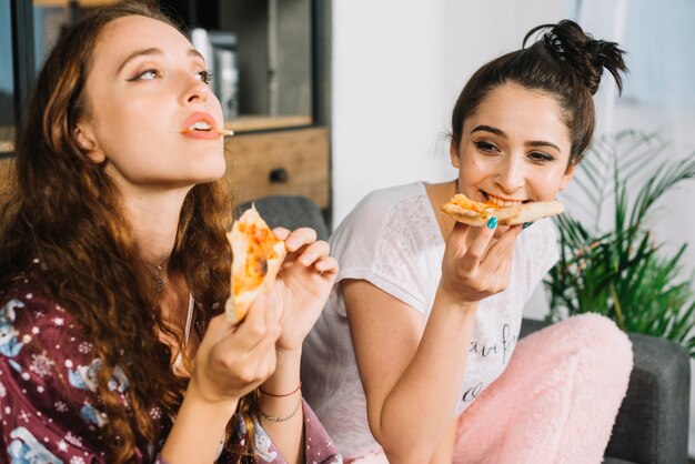 Dos mujeres jóvenes comiendo pizza en casa