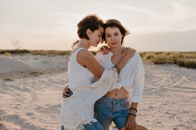 Dos mujeres jóvenes divirtiéndose en la playa al atardecer, romance de amor lesbiana gay