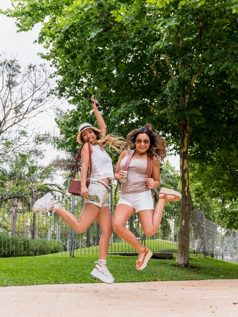 Dos mujeres jóvenes emocionadas que sostienen el mapa y la cámara en la mano que saltan en el aire