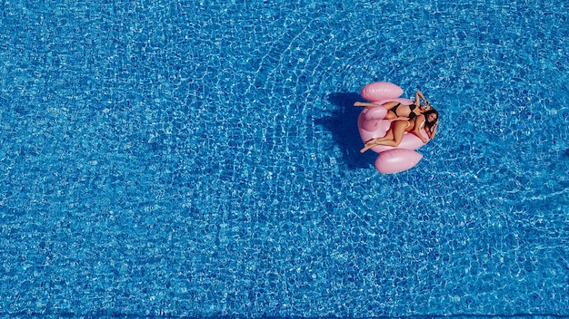 Dos mujeres jóvenes felices con figuras nadan en la piscina de flamencos. Vista superior.