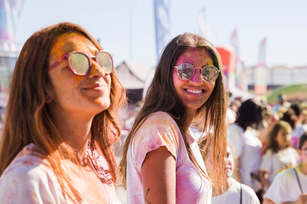 Foto gratuita dos mujeres jóvenes con gafas de sol con polvo holi en la cara