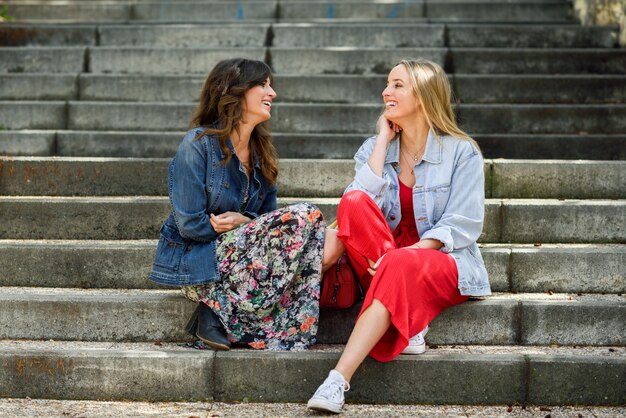Dos mujeres jóvenes hablando y riendo en pasos urbanos.