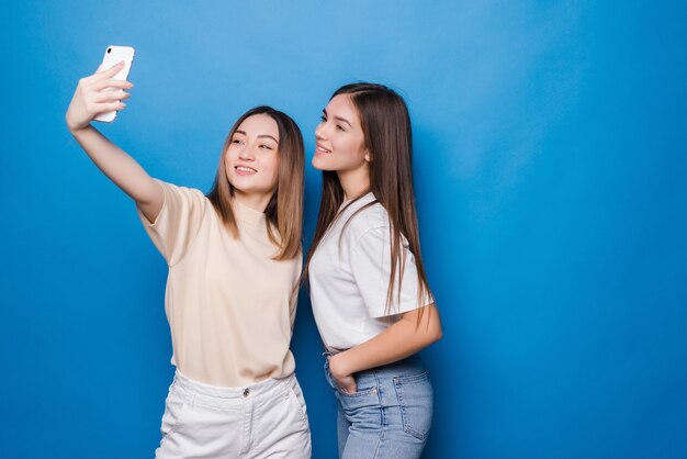 Dos mujeres jóvenes haciendo foto selfie sobre pared azul