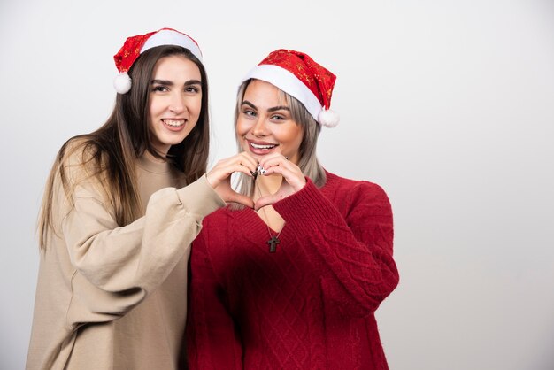 Dos mujeres jóvenes haciendo gesto de símbolo del corazón y riendo.