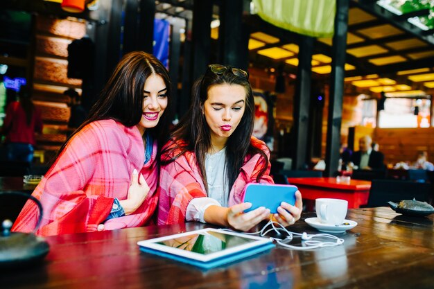 Dos mujeres jóvenes y hermosas sentadas en la mesa y haciendo selfie en el café